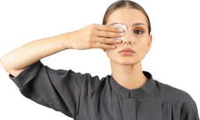 Вид спереди молодой женщины в комбинезоне, снимающей макияж с глаз
