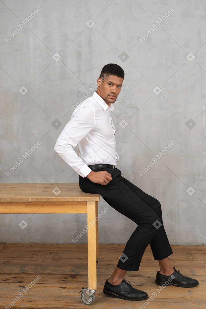 Мужчина в офисной одежде сидит на столе с руками в карманах