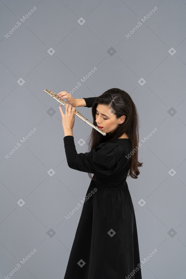 严重的年轻女子，穿着长笛的黑色礼服的侧视图