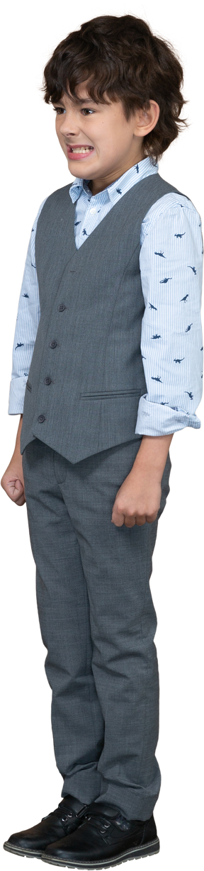Vista frontal de un niño enojado en traje gris de pie con los puños cerrados