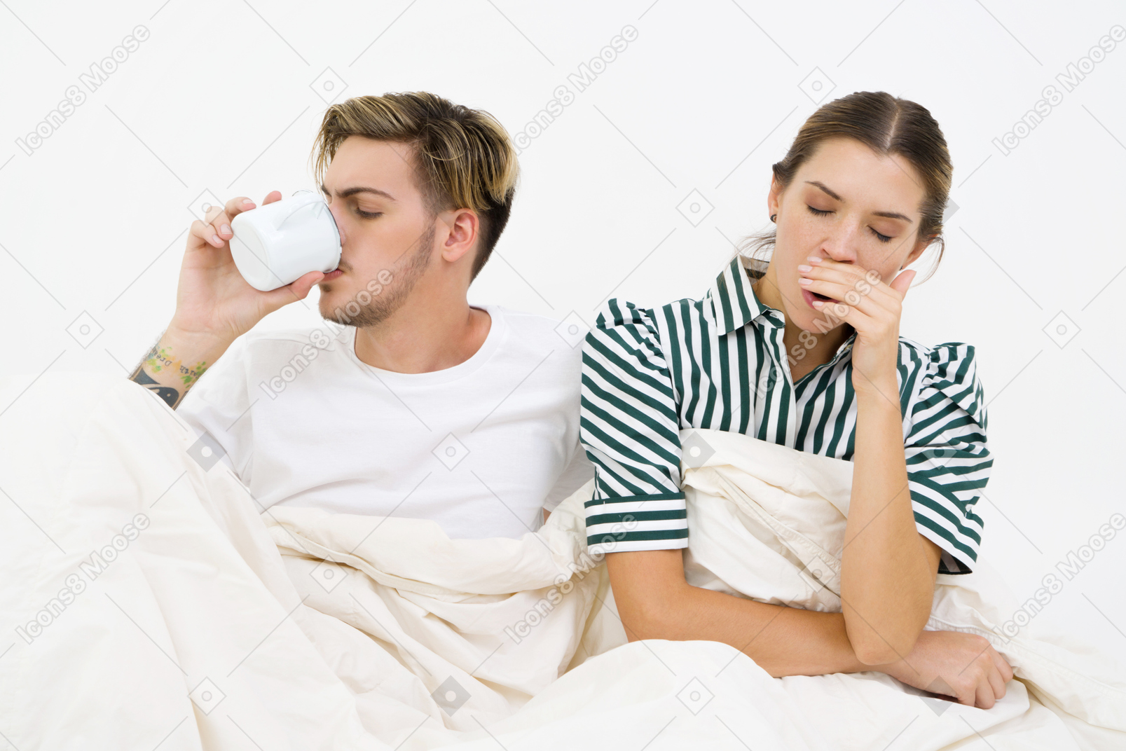 Couple sitting in bed, yawning and drinking coffee