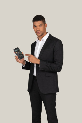 Young man in black suit pointing at calculator he's holding