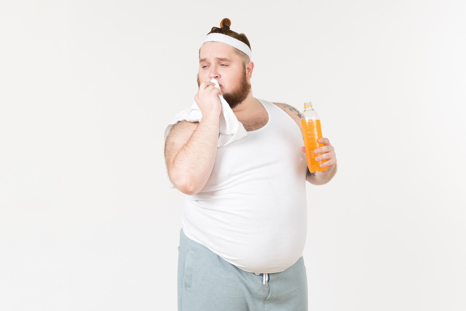 A fat man in sportswear holding a bottle of soft drink and patting his lips dry with a towel