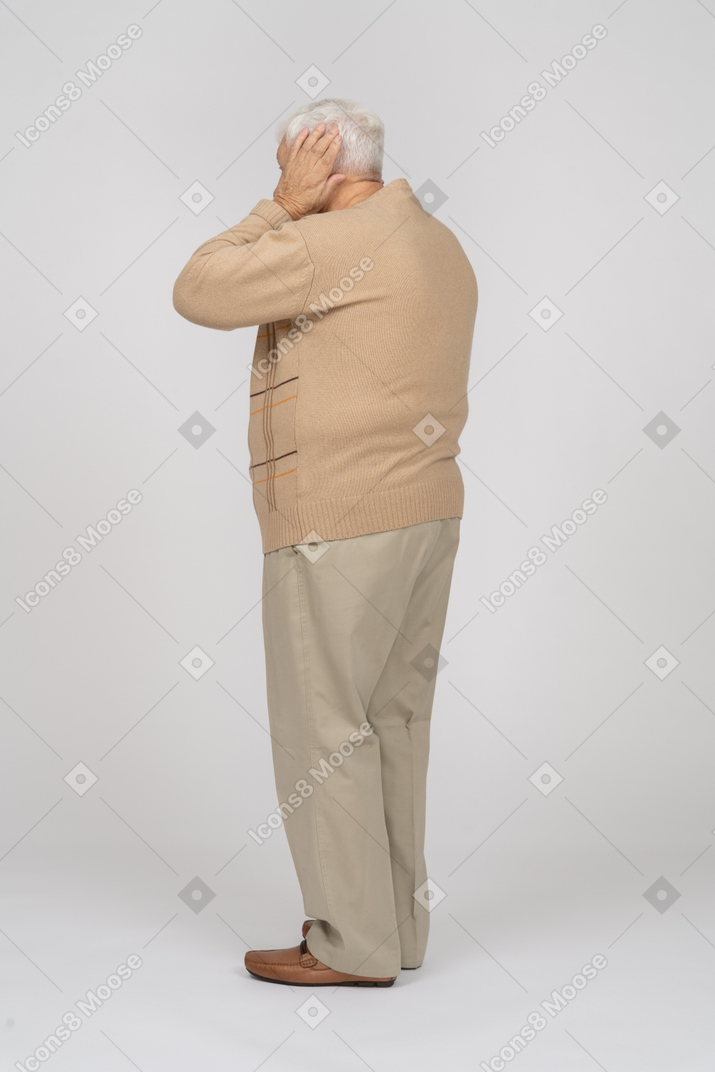 Side view of an old man in casual clothes covering ears with hands