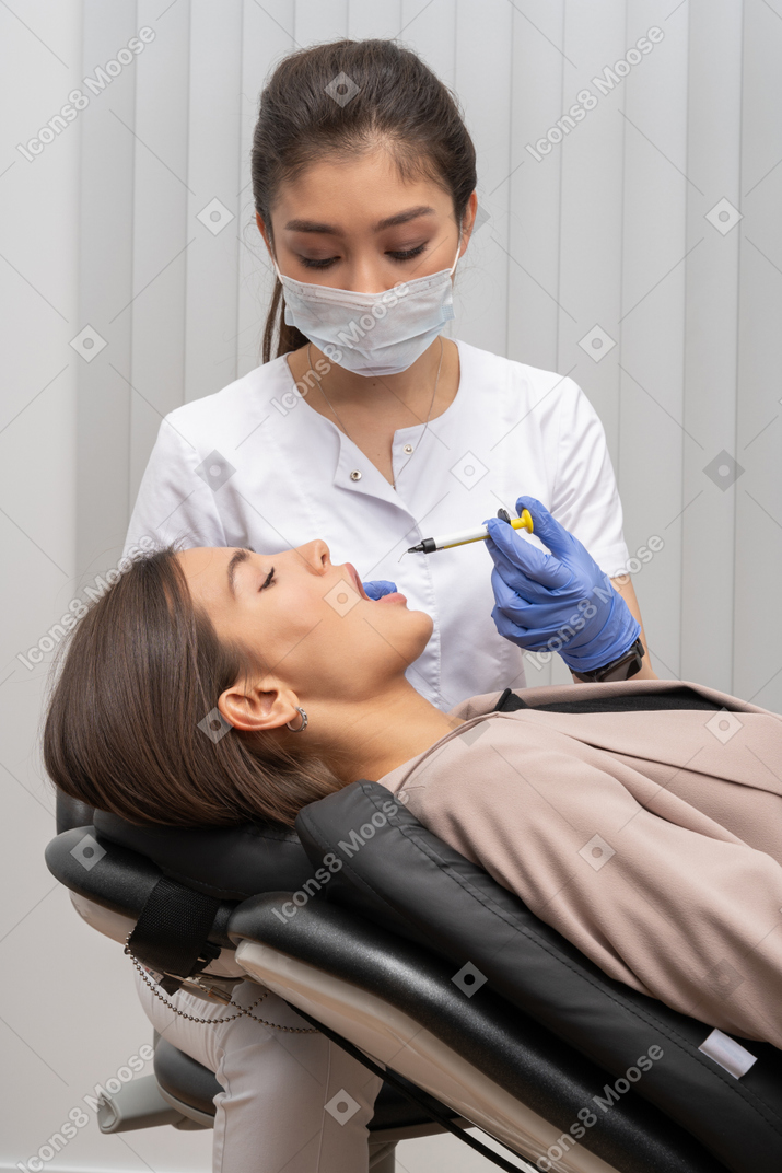 Dentista com máscara e luvas de látex fazendo uma injeção em sua paciente