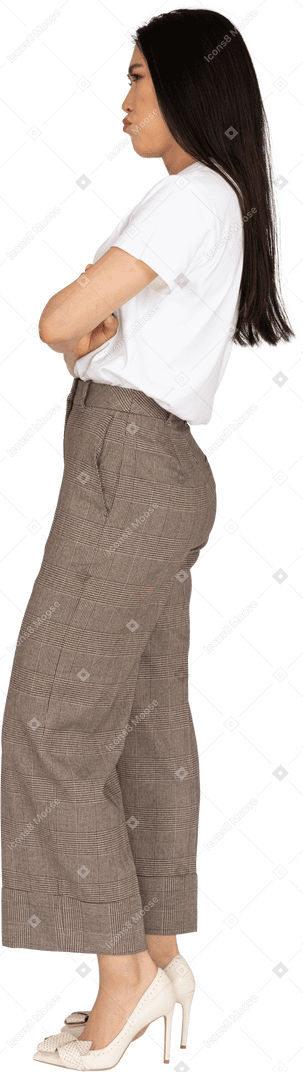 Vista laterale di una giovane donna imbronciata in calzoni e t-shirt attraversando le mani