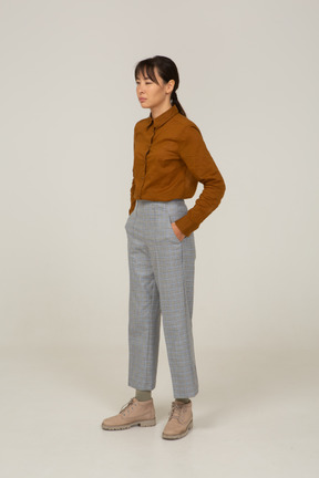 Three-quarter view of a young asian female in breeches and blouse narrowing eyes and putting hands in pockets