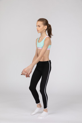 Three-quarter view of a teen girl in sportswear outspreading hands and bending knees