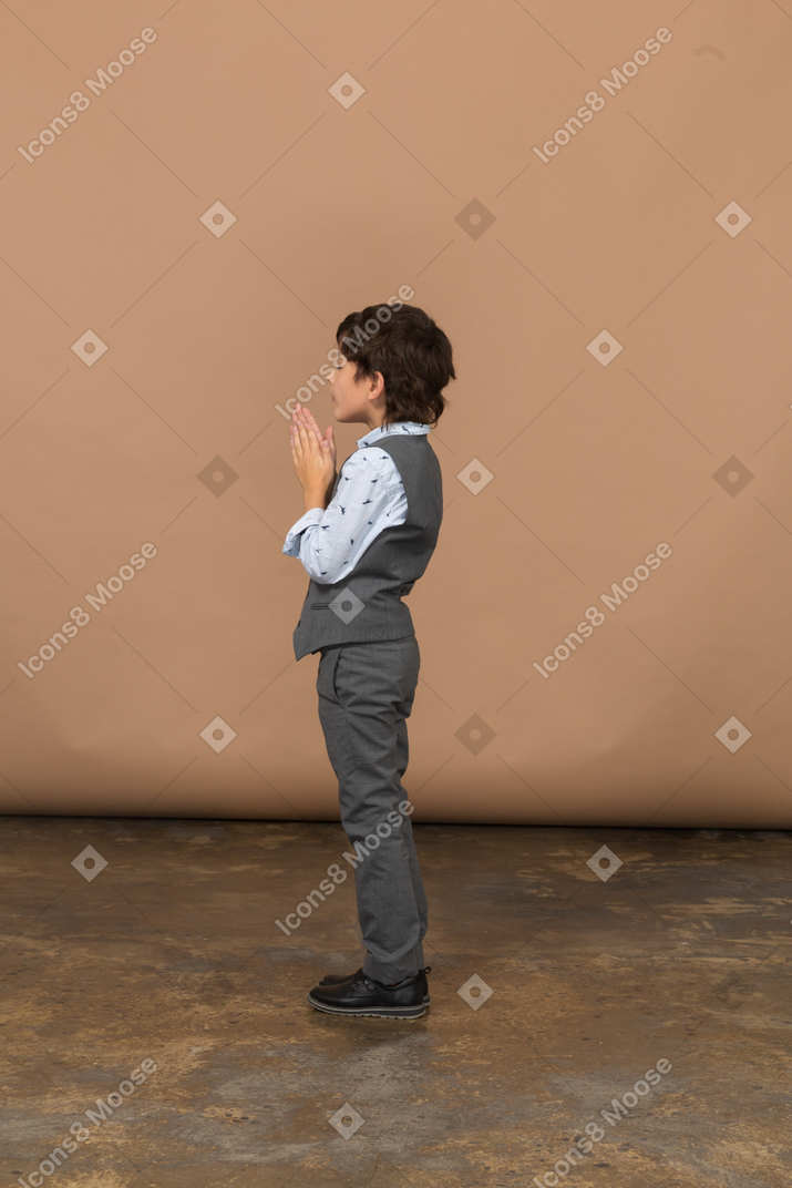 Vue latérale d'un garçon en costume faisant un geste de prière