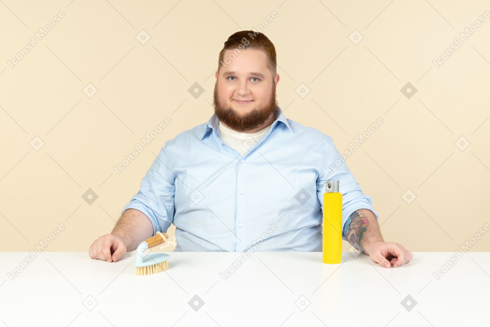 Zufrieden aussehender junger übergewichtiger hausmann sitzt am tisch mit reinigungsspray und pinsel drauf