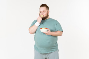 Tipo grande en ropa deportiva comiendo hojas de ensalada que ha recogido del plato