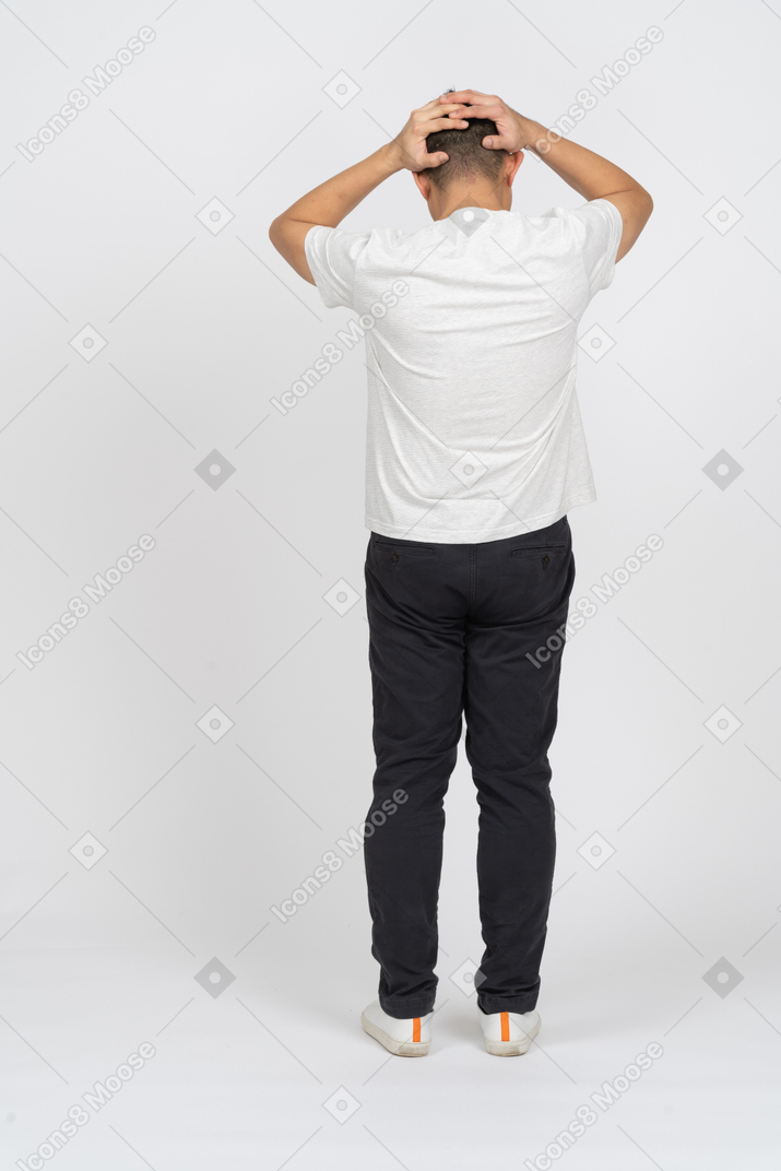 頭に手を置いて立っているカジュアルな服装の男の背面図