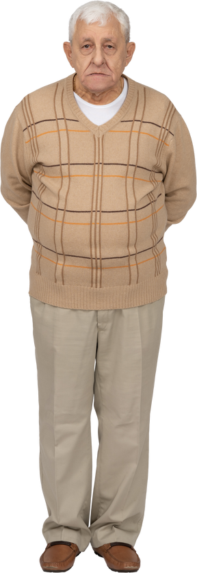 Vista frontal de un anciano con ropa informal de pie con las manos detrás de la espalda y mirando a la cámara