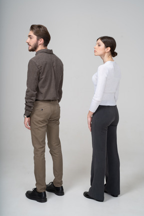 Three-quarter back view of a young couple in office clothing raising head