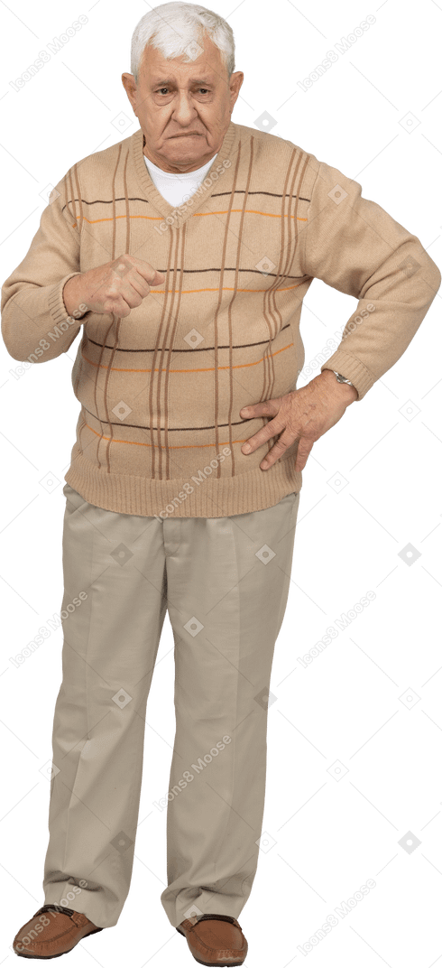 Vue de face d'un vieil homme en vêtements décontractés debout avec la main sur la hanche et regardant la caméra