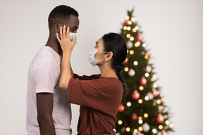 A man and a woman wearing face masks in front of a christmas tree