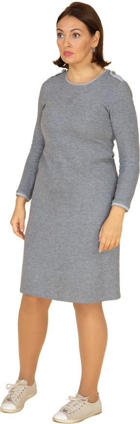 Vue de face d'une femme en robe grise debout avec les bras croisés