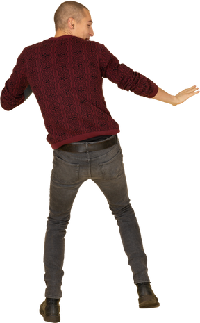 Back view of a scared unwilling young man dressed in red pullover outstretching his hands