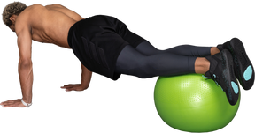 一个赤膊的非洲人在健身球上做俯卧撑的四分之三后视图