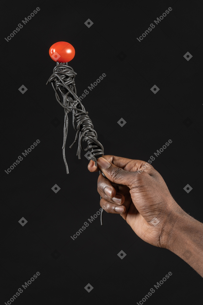 Close-up of a human hand holding black pasta with cherry tomato