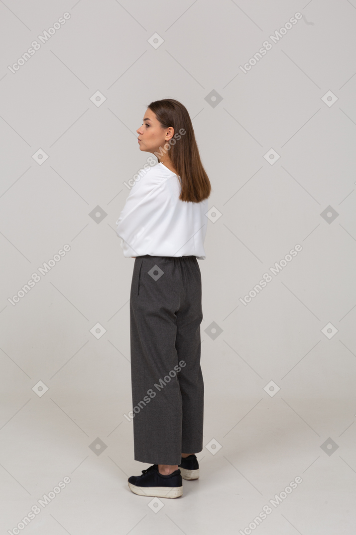 Vista posteriore di tre quarti di una giovane donna in abiti da ufficio che incrociano le braccia