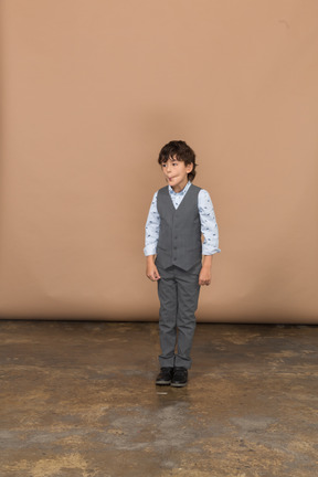 Vista frontal de un niño en traje parado y haciendo muecas