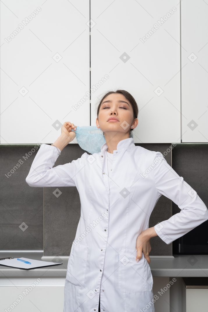 Вид спереди усталой женщины-врача, поднимающей руку с закрытыми глазами