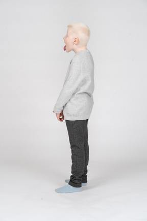 Vista laterale di un ragazzino in abiti casual che mostra la lingua