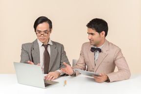 Zwei junge nerds, die am tisch sitzen und geräte benutzen