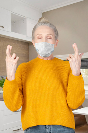 Elderly woman with crossed fingers wearing a face mask