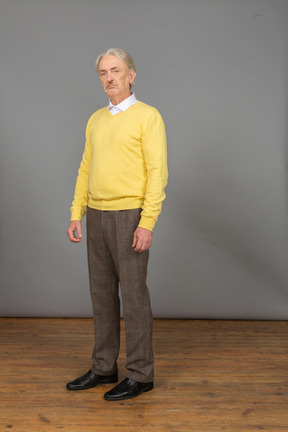 Vista de tres cuartos de un anciano disgustado vistiendo jersey amarillo y mirando a la cámara