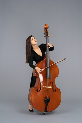 Vista frontale di una giovane donna in abito nero che suona il contrabbasso con un arco mentre guarda in alto