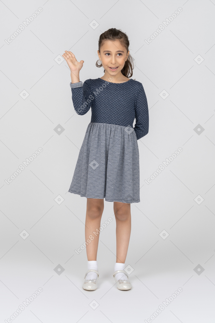 Vista frontal de uma garota acenando com a mão com um sorriso tímido