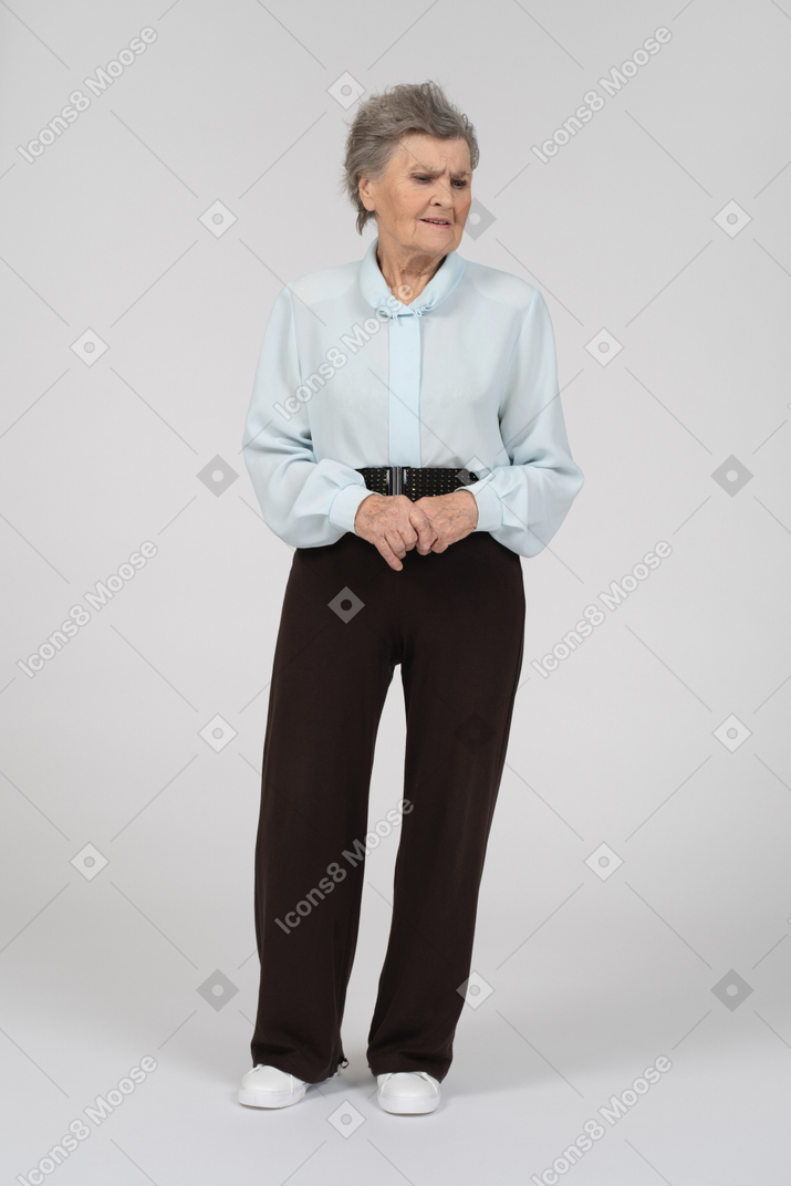 Vista frontal de una anciana mirando hacia abajo con preocupación y manos entrelazadas