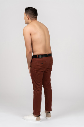 Three-quarter back view of a shirtless latino man hunching a little