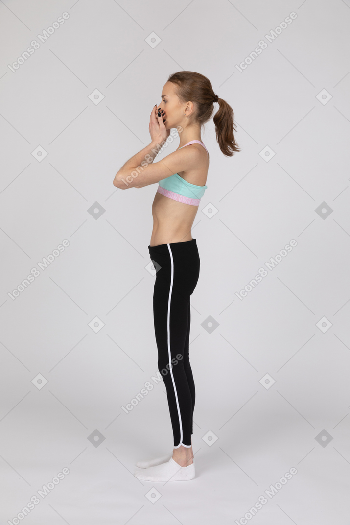 Vista lateral de uma adolescente em roupas esportivas cobrindo a boca