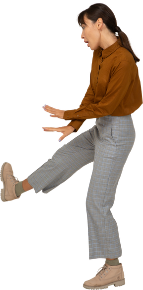 一位身着马裤和上衣抬腿跳舞的亚洲年轻女性的侧视图