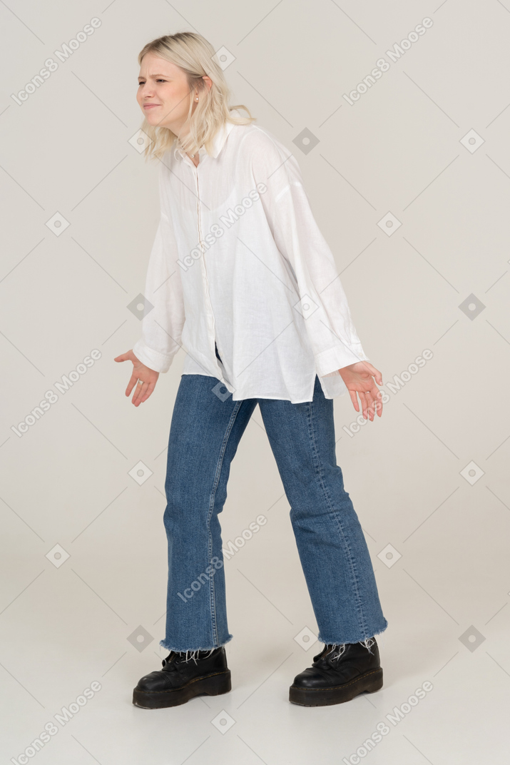 Vista di tre quarti di una donna bionda in abiti casual che fa smorfie e allarga le braccia