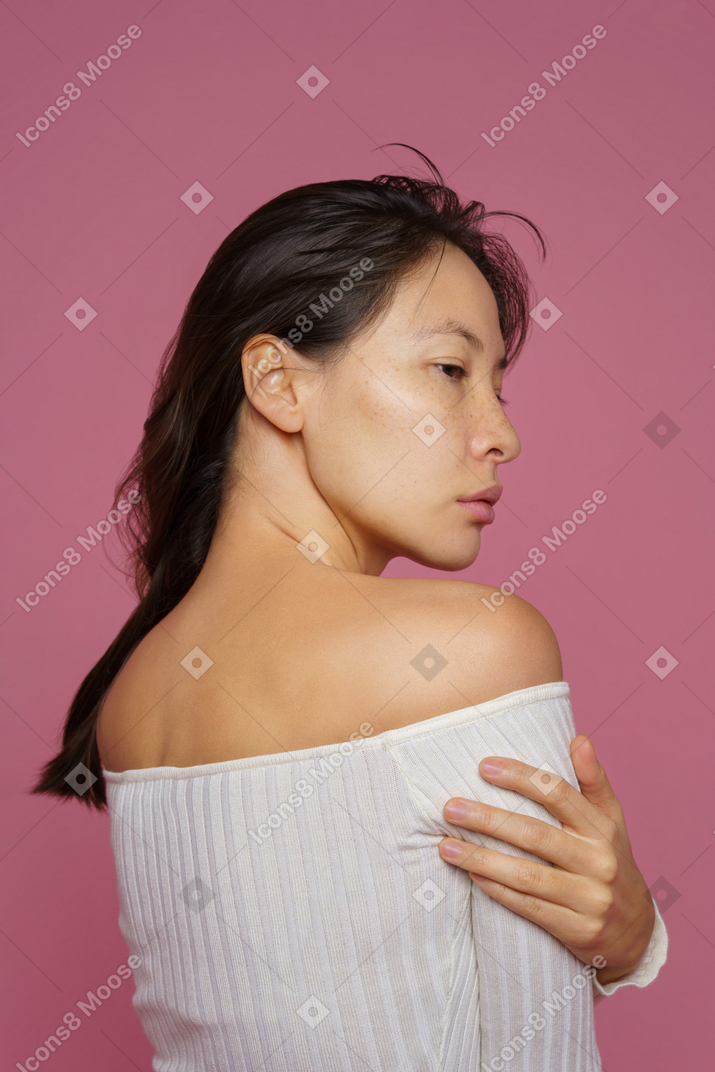 Трехчетвертный вид сзади темноволосой женщины, касающейся плеча и смотрящей в сторону
