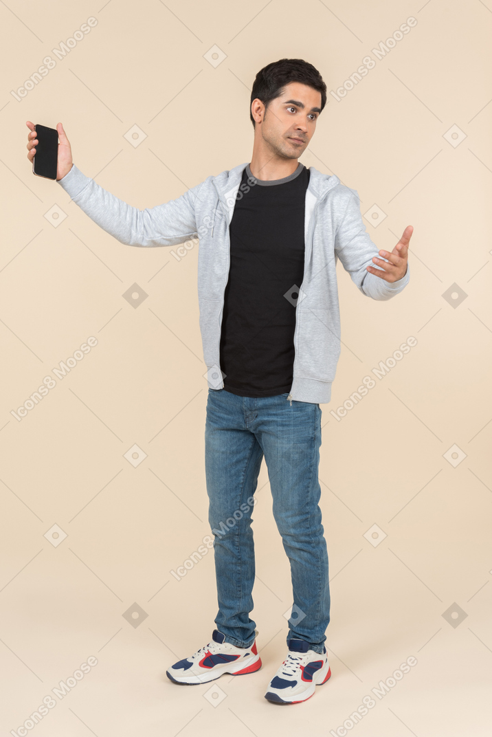 Joven hombre caucásico apuntando al teléfono inteligente que está sosteniendo
