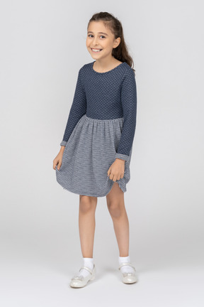 Vista frontal de una niña sosteniendo el dobladillo de su falda con una amplia sonrisa