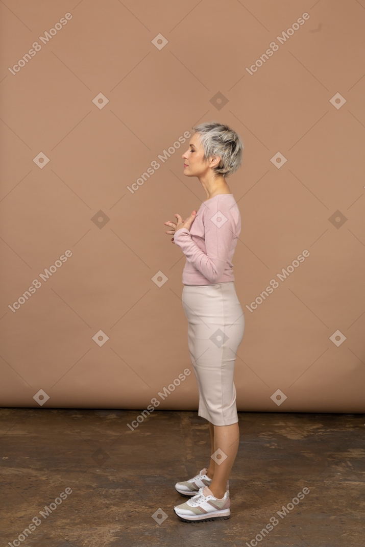 Vista lateral de uma mulher com roupas casuais, posando com as mãos no peito