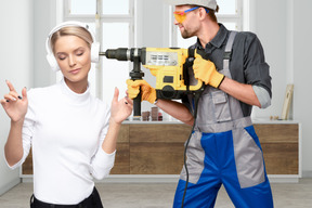 Woman in headphones standing next to worker with demolition hammer