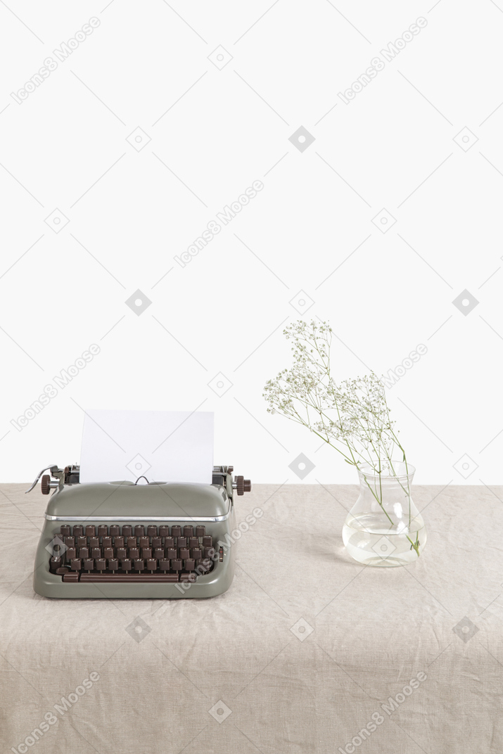 Glass vase with twig and vintage typewriter on the table