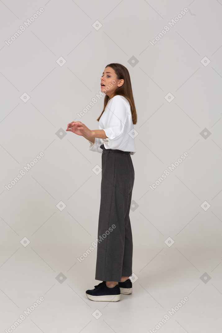 Side view of a shocked young lady in office clothing raising hands
