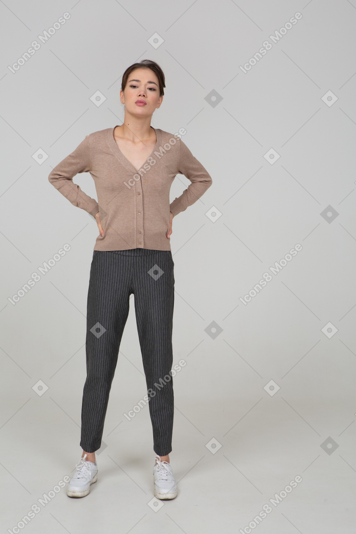 Front view of a displeased young lady in pullover and pants putting hands on hips and looking aside