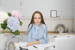 A woman sitting at a table with blueprint, laptop and vase of flowers