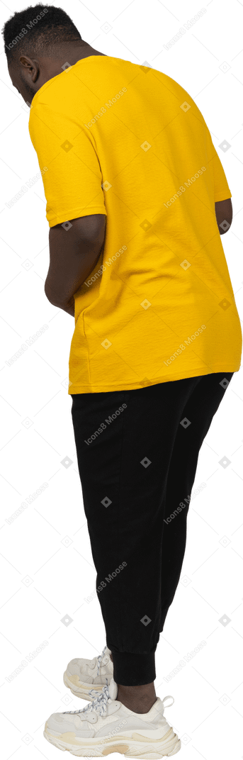 Three-quarter back view of a young dark-skinned man in yellow t-shirt touching stomach & looking down