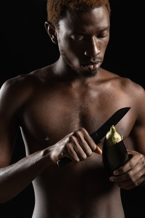Close-up a naked young man cutting an eggplant