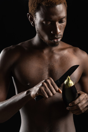 Nahaufnahme eines nackten jungen mannes, der eine aubergine schneidet